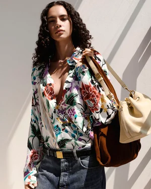 Model wearing a multicolor floral print shirt and blue jeans with a cream bucket bag and brown suede shoulder bag in Missoni SS26.