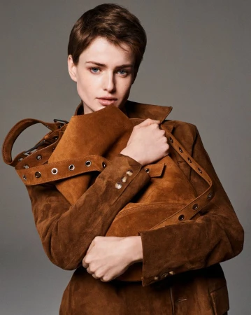 Model Lando van der Schee holding a brown suede bag while wearing a matching brown suede jacket against a grey backdrop.