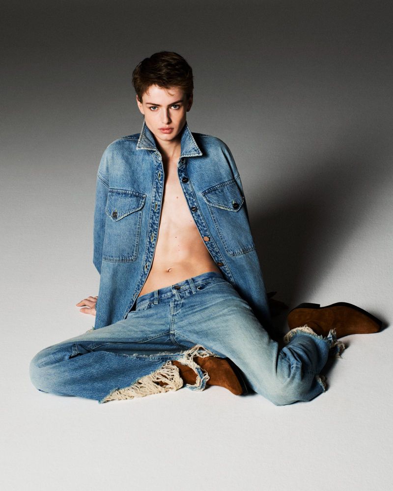 Model Lando van der Schee seated on a studio floor wearing an open denim jacket, frayed jeans, and brown suede boots.