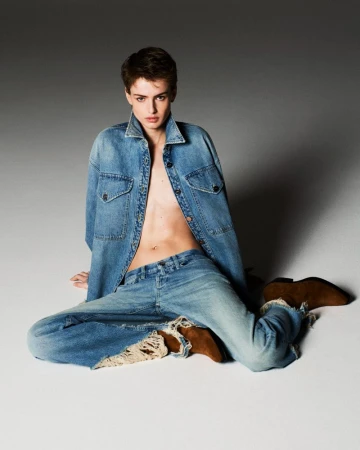Model Lando van der Schee seated on a studio floor wearing an open denim jacket, frayed jeans, and brown suede boots.