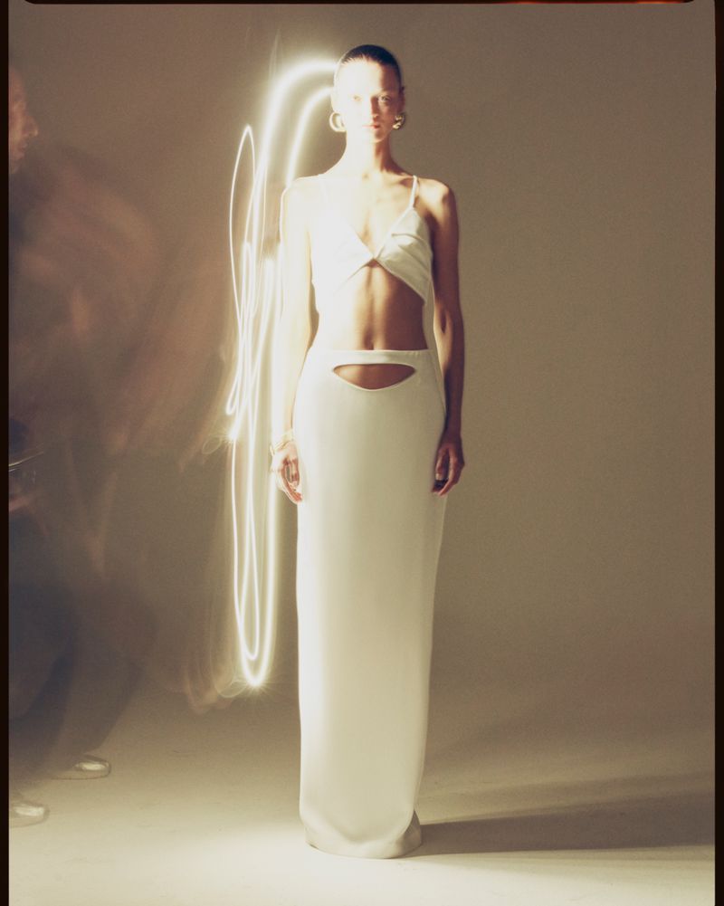 Elegant adult woman in a light cream dress with center cut-out, posing in a studio with a light effect. Fashion photography.