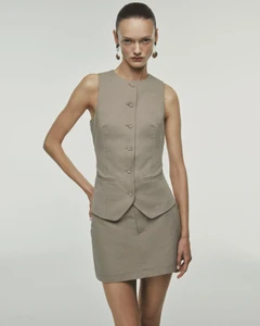 Model wearing a neutral taupe buttoned vest and matching skirt against a plain studio background.