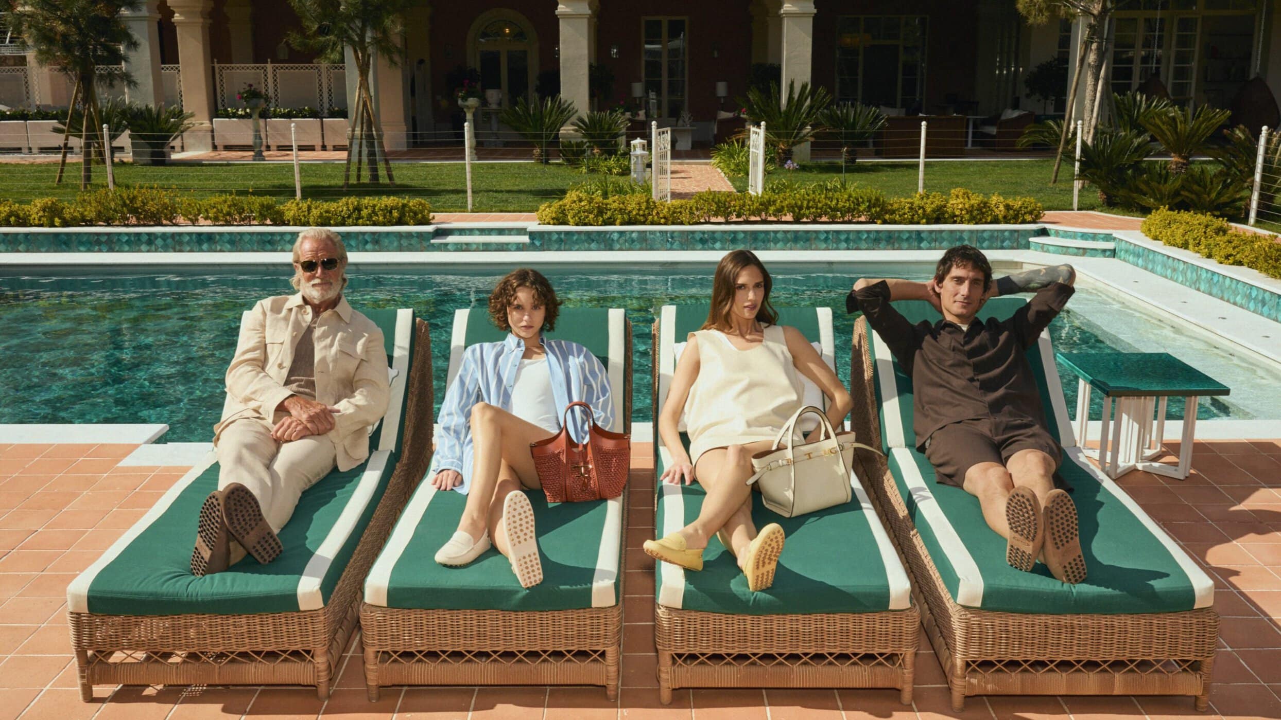 Four models lounging on green-cushioned sunbeds by a tiled swimming pool for Tod's Vacanze Italiane campaign