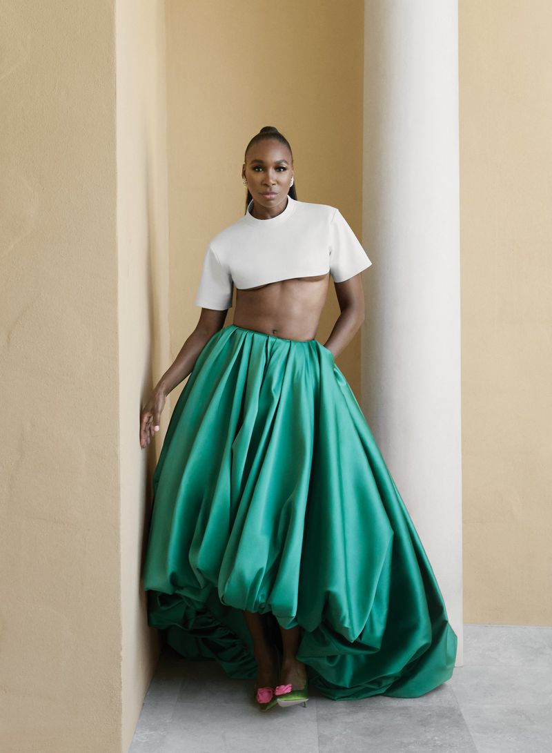 Venus Williams poses in a white crop top and voluminous emerald green satin skirt beside a white column.