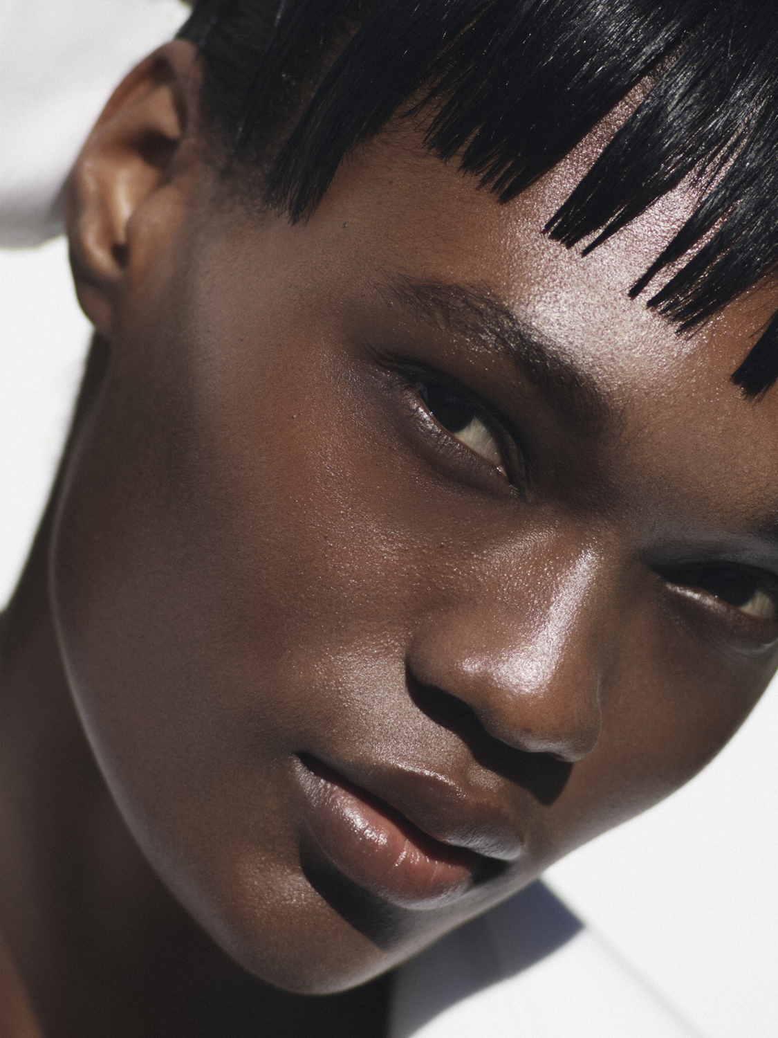 Close-up portrait of a young Black woman with short black hair, a subtle smile, and natural makeup against a soft, white backdrop.