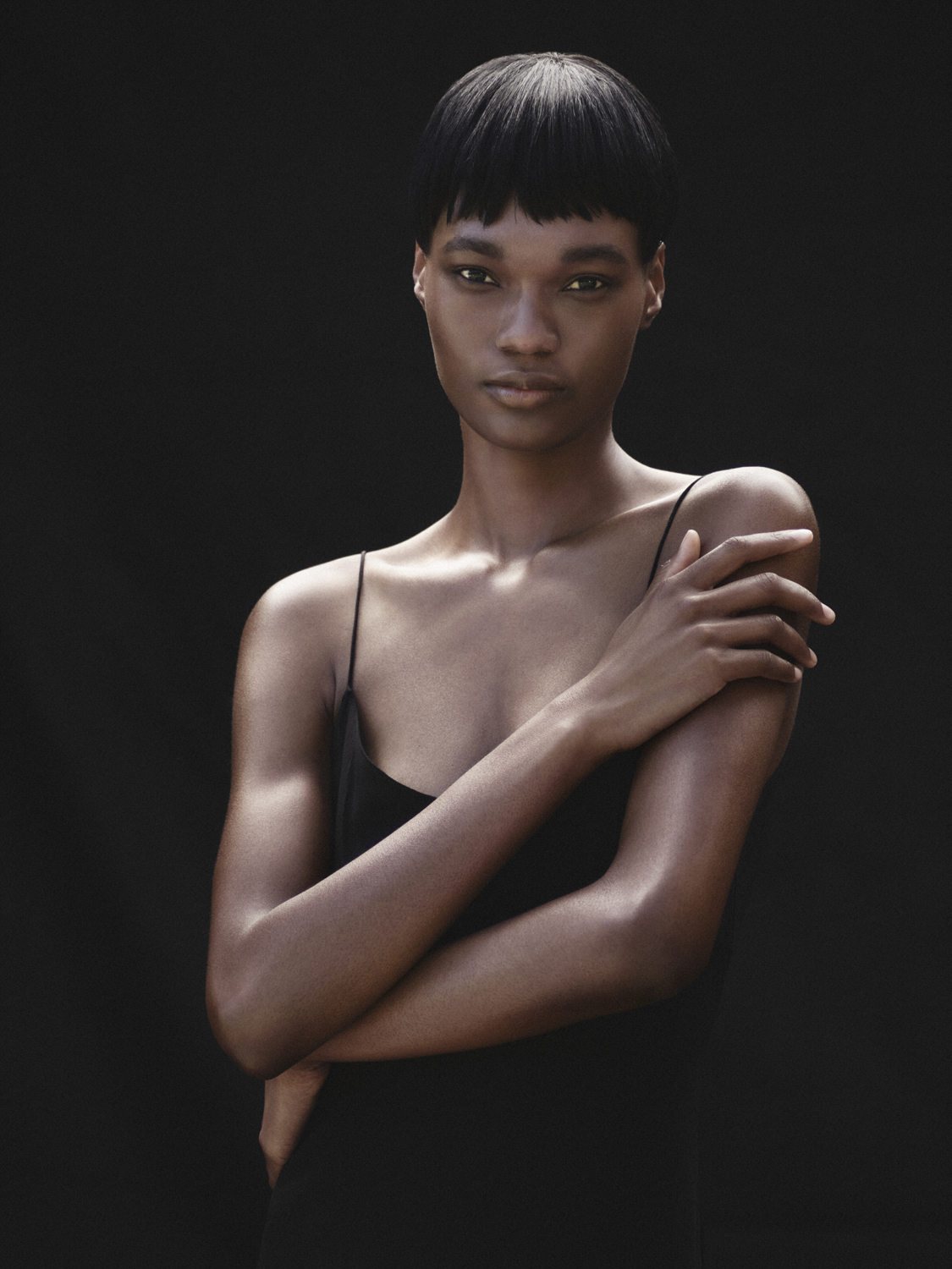 Portrait of an African American woman with crossed arms against a dark background. Close-up of a person in simple studio lighting.