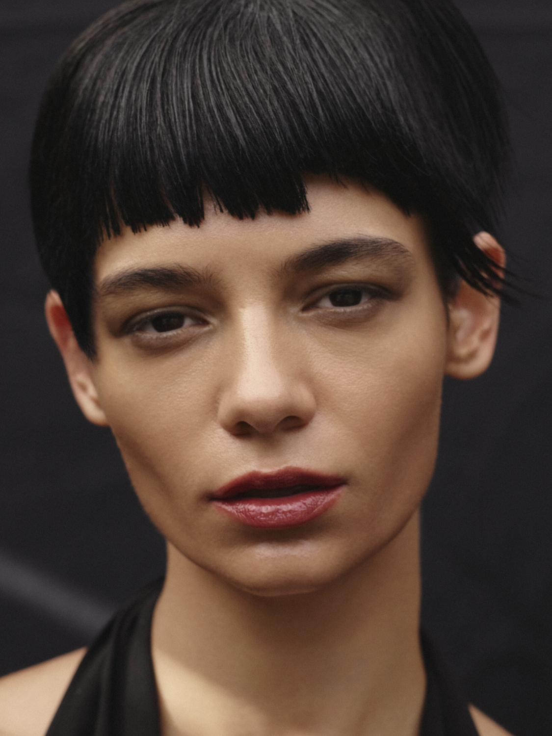 Close-up portrait of a young adult female with fair skin, dark eyes, short black hair and glossy red lips, wearing a black halter top.