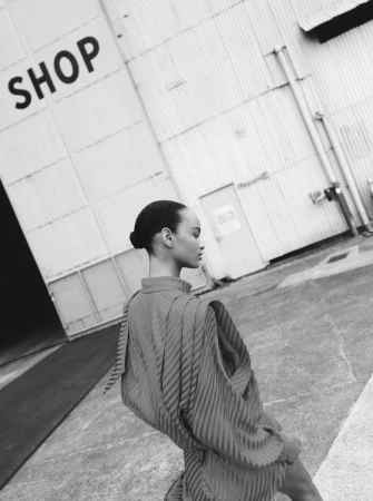 A stylish adult woman is shown outdoors in a monochrome fashion shot, showcasing a textured dress against a building backdrop.
