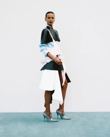 Model Liya Kebede wearing a deconstructed black and white layered outfit with pointed stiletto heels against a white studio backdrop.