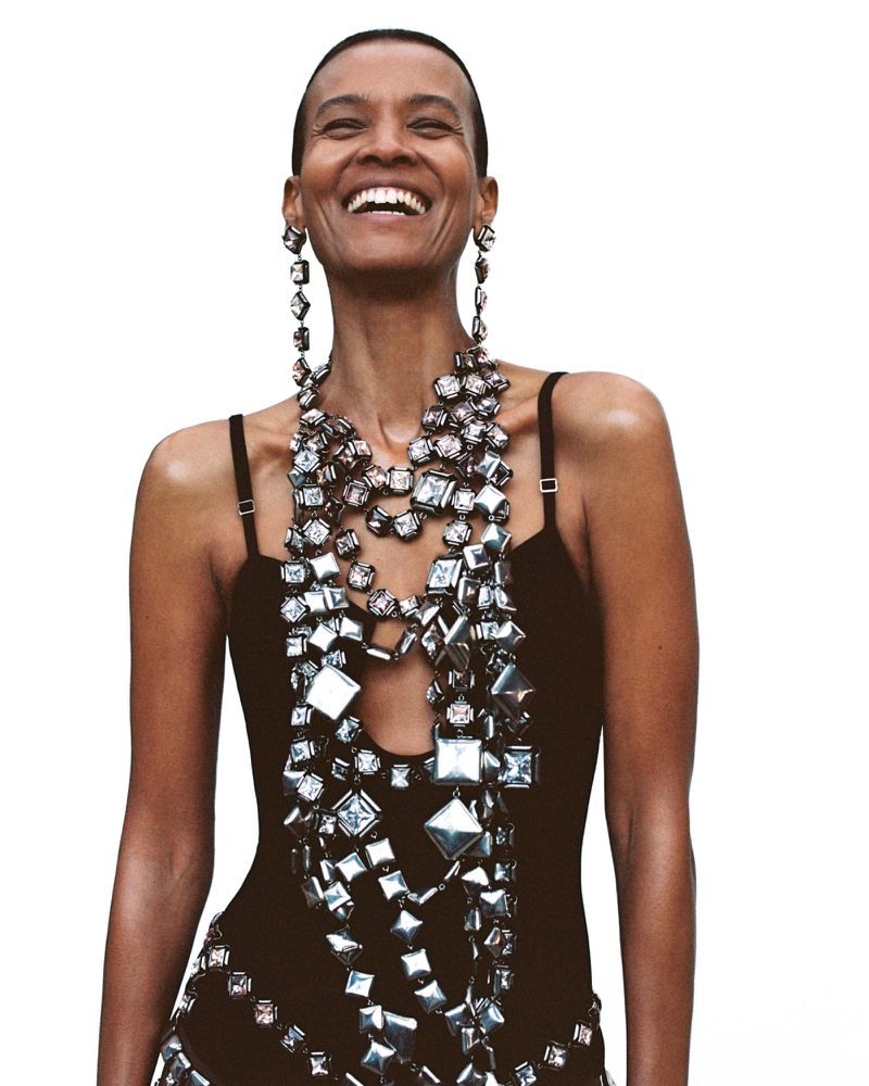 Model Liya Kebede laughing in a black strap top and heavy metallic geometric statement jewelry against a white background.