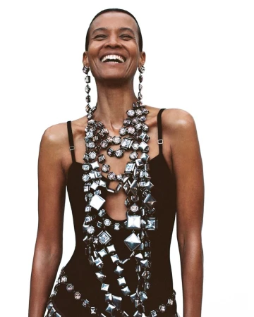 Model Liya Kebede laughing in a black strap top and heavy metallic geometric statement jewelry against a white background.