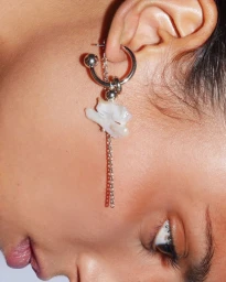 Close-up portrait of an ear wearing a silver barbell hoop earring with dangling chain and white pearl pendant.