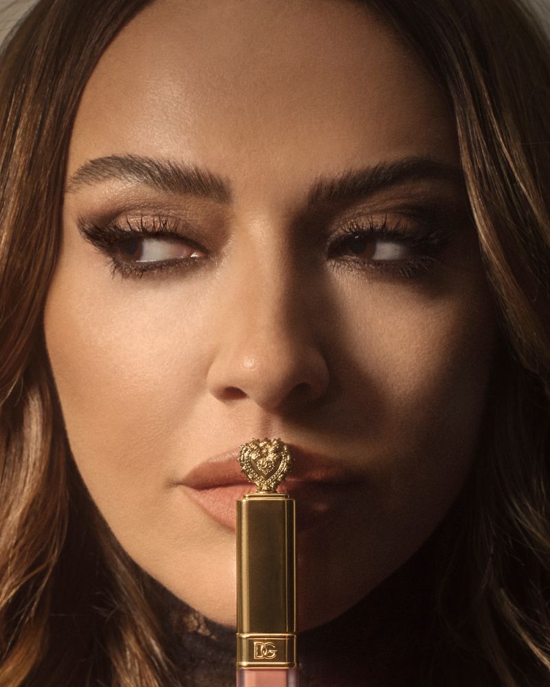 Close-up portrait of Hadise holding a gold lipstick tube vertically against her lips for Harper's Bazaar Turkey