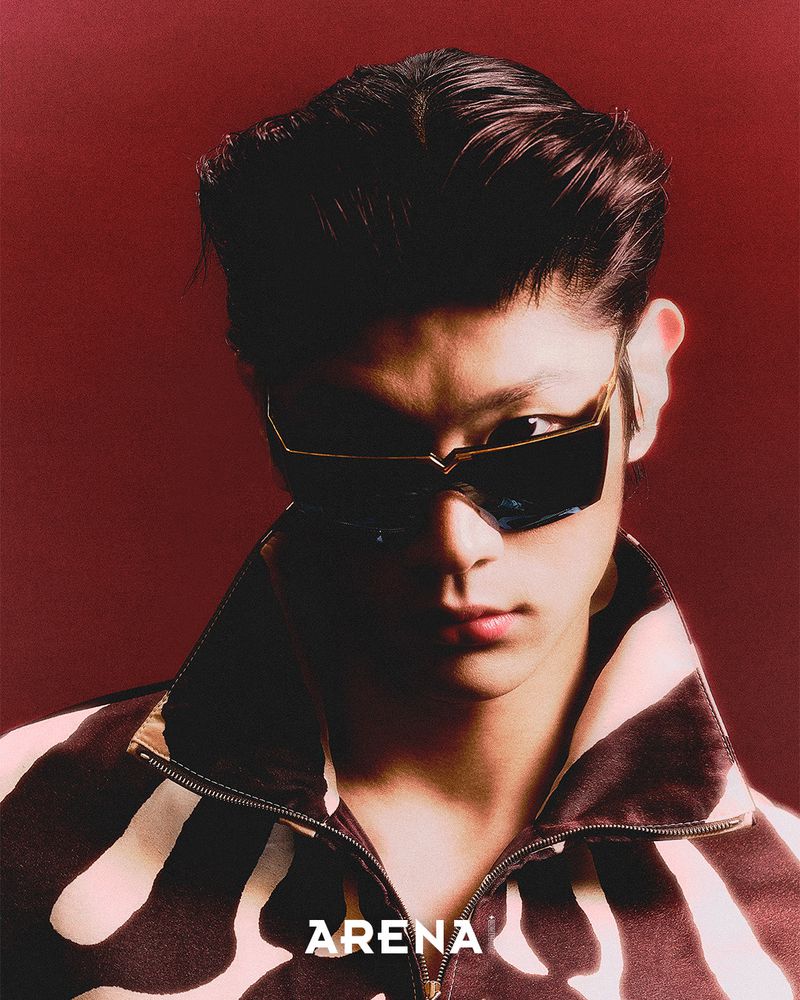 Portrait of a man wearing dark sunglasses and a patterned zipped jacket against a deep red background for Arena Homme Plus Korea.
