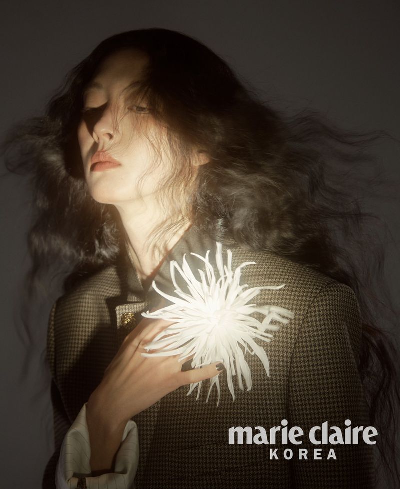 Model So Young Kang with flowing dark hair wearing a patterned blazer and a large white floral brooch for Marie Claire Korea.