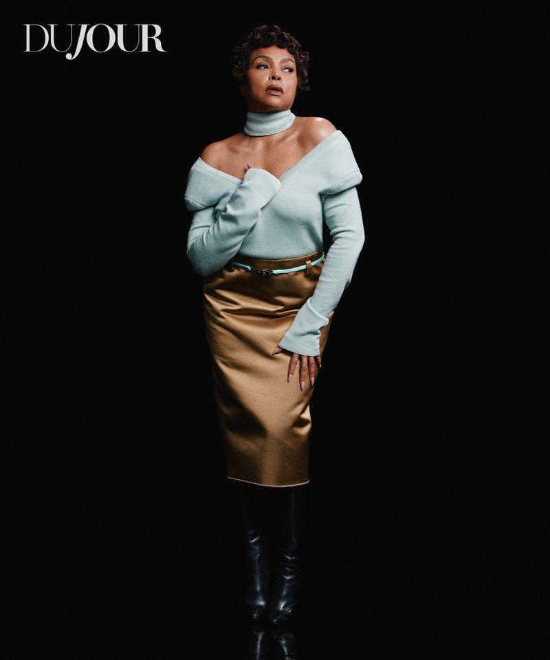 Taraji P. Henson posing in an off-shoulder pale blue top and metallic gold satin midi skirt against a black background.