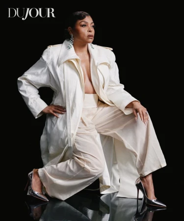 Taraji P. Henson posing in an ivory trench coat, wide-leg trousers, and metallic silver stiletto heels against a black backdrop.