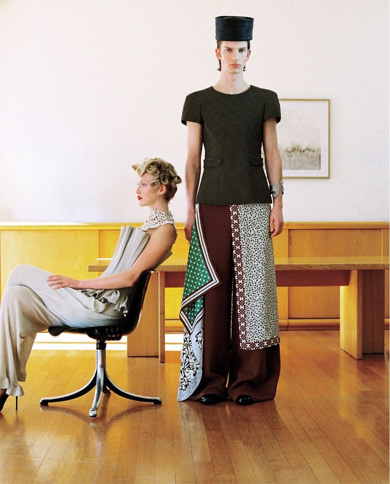 A man standing and a woman seated in a room with wooden floors, photographed for Numero Netherlands project Exaggeration.
