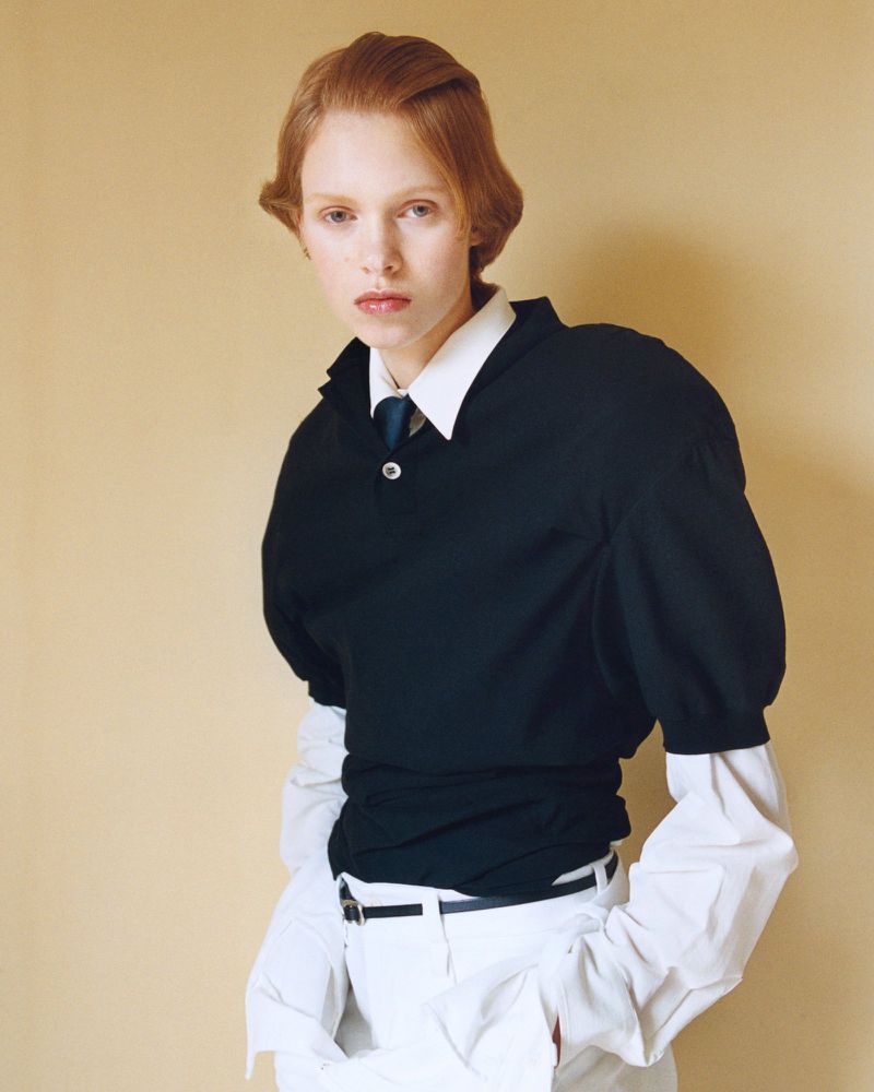Model Nanne Groenewegen wearing a black short-sleeve polo layered over a white collared shirt against a beige studio backdrop.