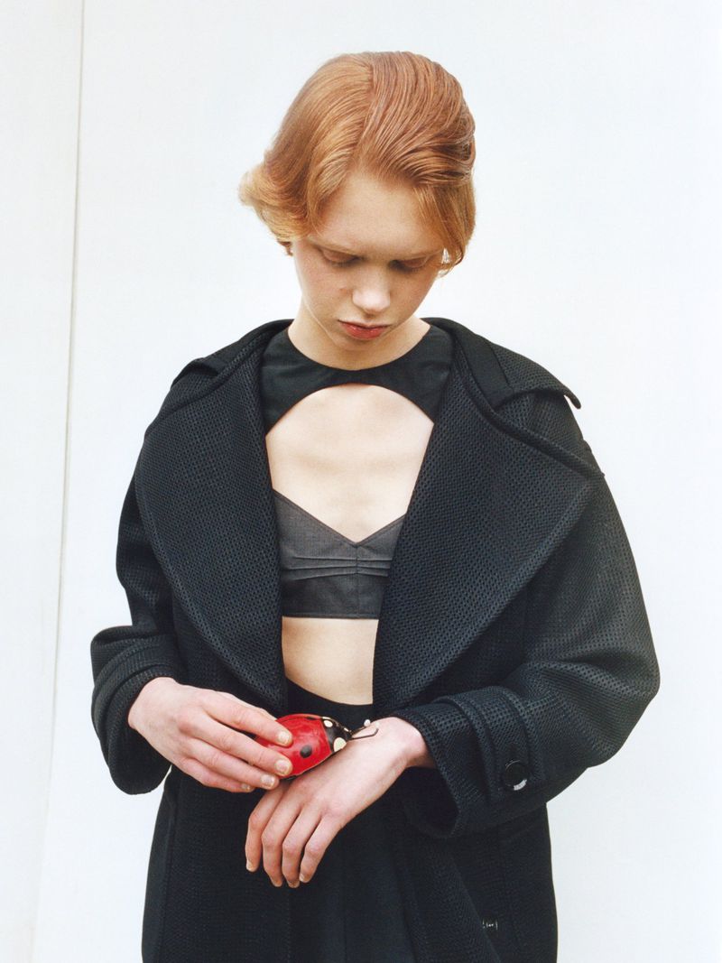 Model Nanne Groenewegen in an open black textured coat holding a red ladybug object against a plain white background.
