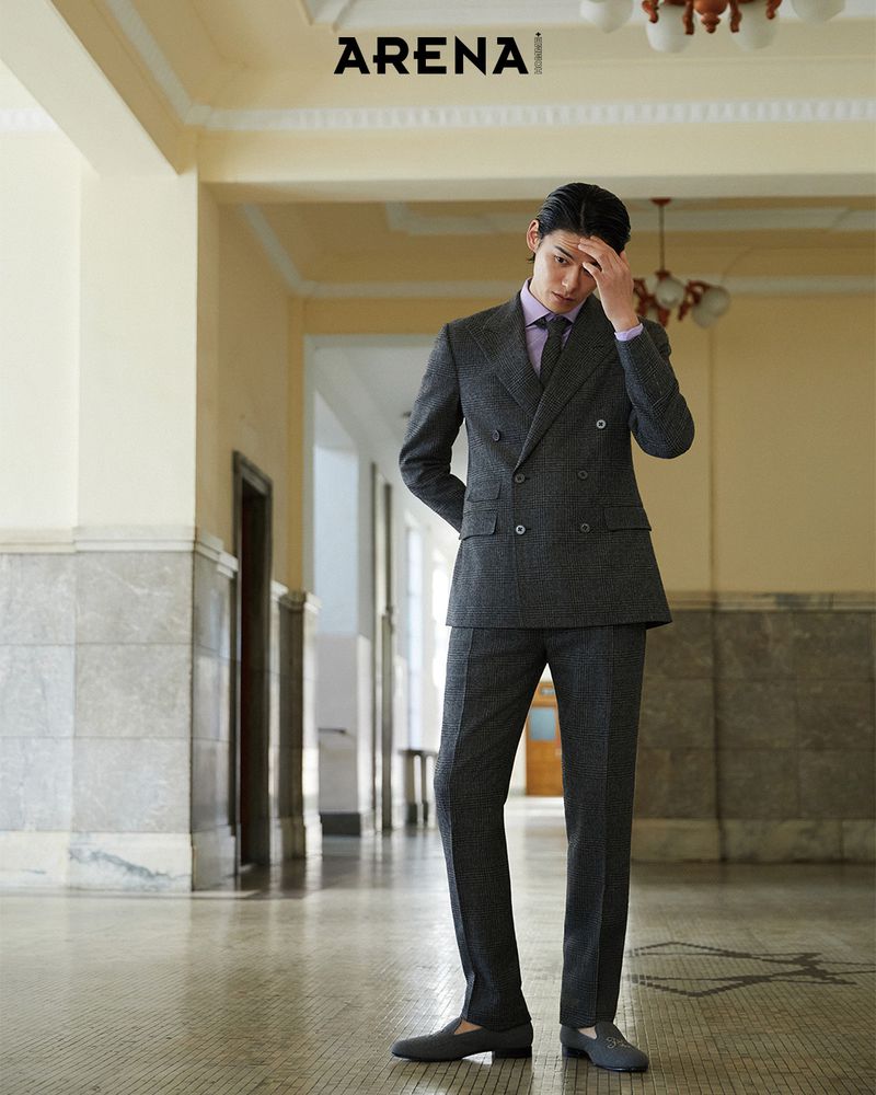 Kim Won wearing a charcoal double-breasted suit and lavender shirt posing in a classic tiled hallway.