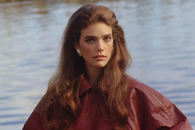 Model Betsy Gaghan wearing a reddish-brown leather jacket and silver earring with rippling water in the background.
