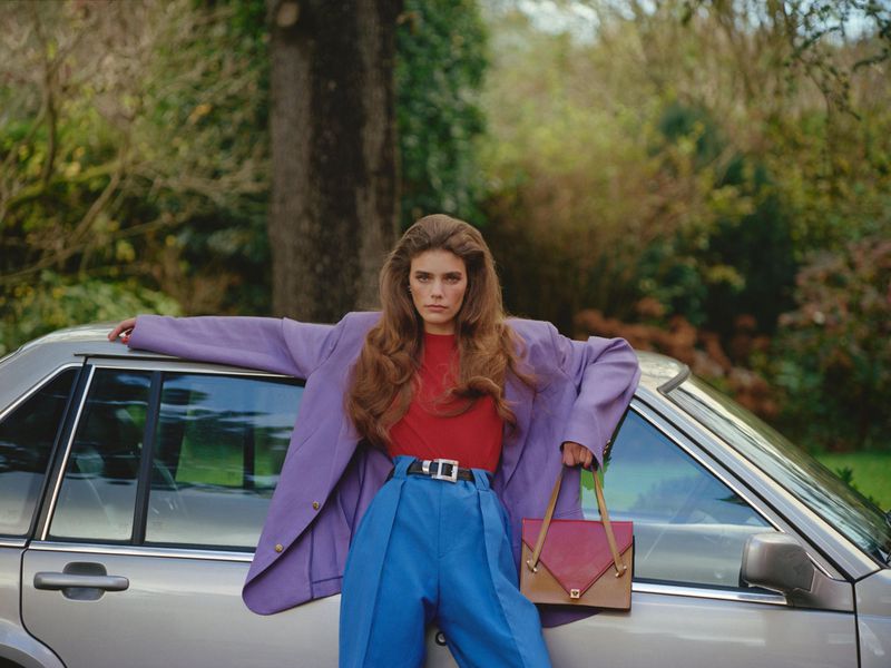 Model Betsy Gaghan posing in an oversized purple blazer and blue trousers against a silver car for D Repubblica.