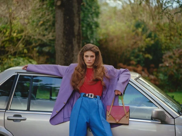Model Betsy Gaghan posing in an oversized purple blazer and blue trousers against a silver car for D Repubblica.