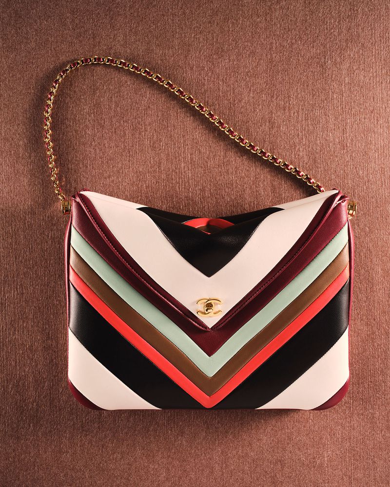 Multicolor chevron striped leather handbag with a gold chain strap displayed on a textured brown surface.