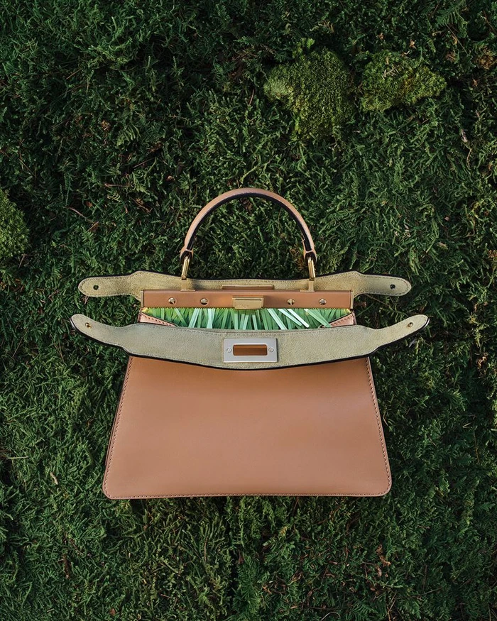 Tan leather handbag resting open on a textured bed of green moss in a top-down view.