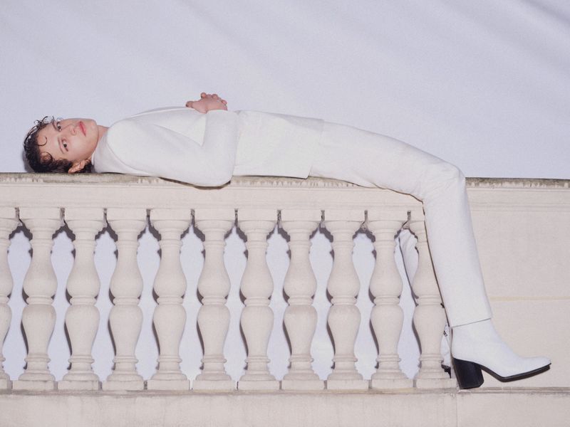 Model Siegfried Blanche in an all-white suit lying horizontally across a classical stone balustrade.