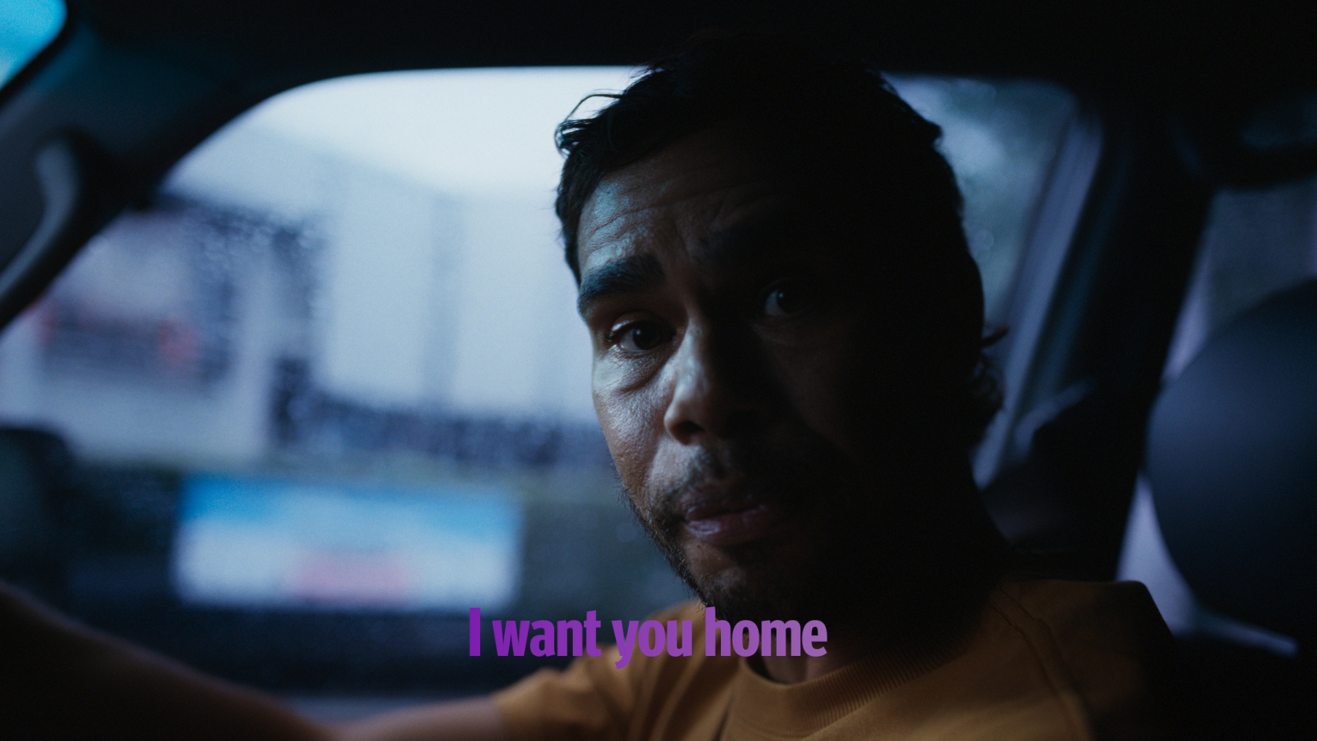 Portrait of an adult man inside a car at night with blurred city lights in the background; he is partially lit.