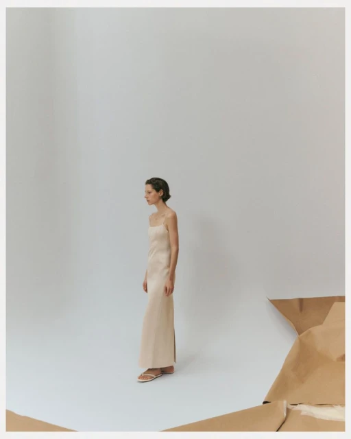 Elegant woman in a champagne-colored dress posing in a studio, neutral tones, clean aesthetic fashion portrait, minimalist style.