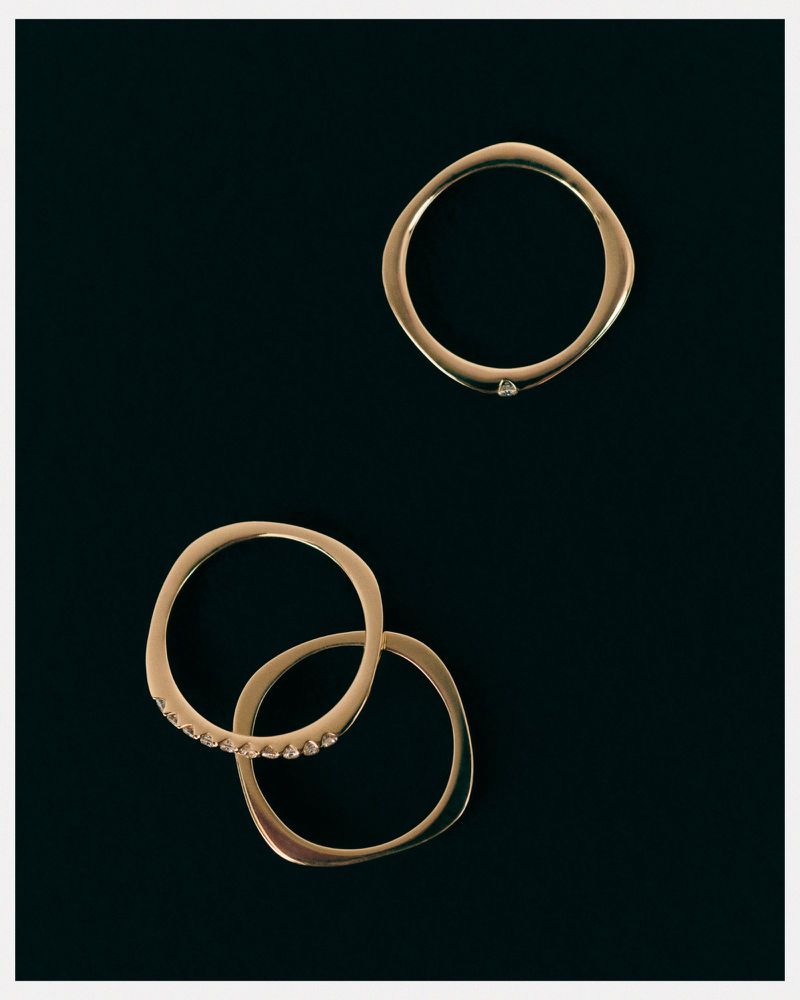 Three gold, rounded rings are displayed on a dark background, one featuring small diamonds, arranged in an aesthetic composition.