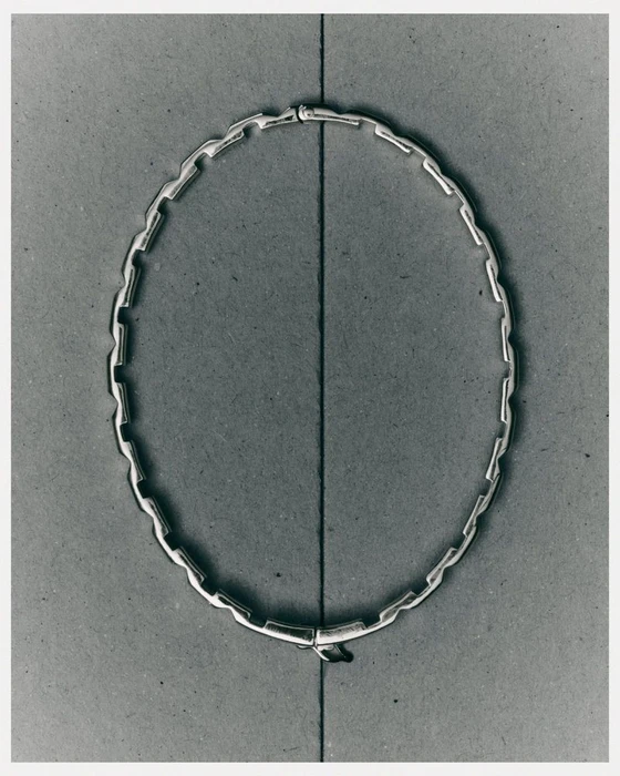 Silver linked choker necklace displayed flat on a dark textured grey paper background with a vertical dividing crease line