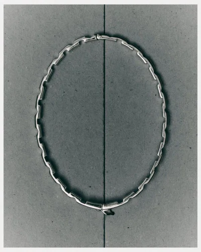 Silver linked choker necklace displayed flat on a dark textured grey paper background with a vertical dividing crease line