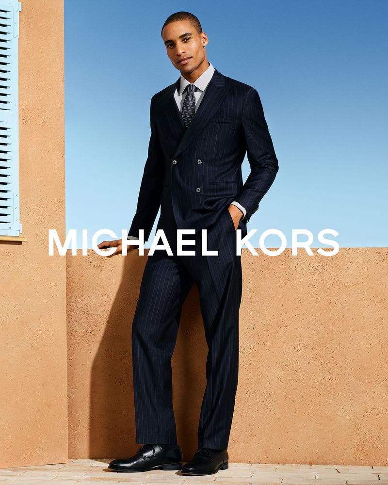 Man wearing a navy pinstripe suit and tie standing against a terracotta wall under a clear blue sky