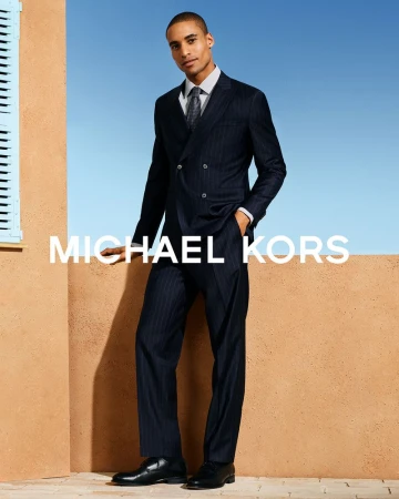 Man wearing a navy pinstripe suit and tie standing against a terracotta wall under a clear blue sky
