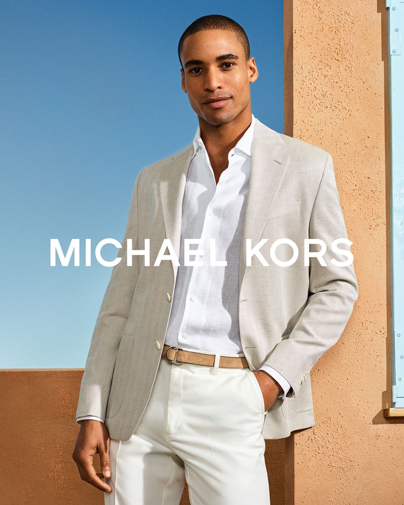 Model Malik Lindo wearing a tailored beige blazer, white shirt, and white trousers in the Michael Kors S/S 26 campaign.