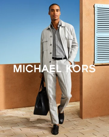 Model Malik Lindo wearing a grey linen jacket and trousers while carrying a black leather bag on a sunlit terracotta terrace.
