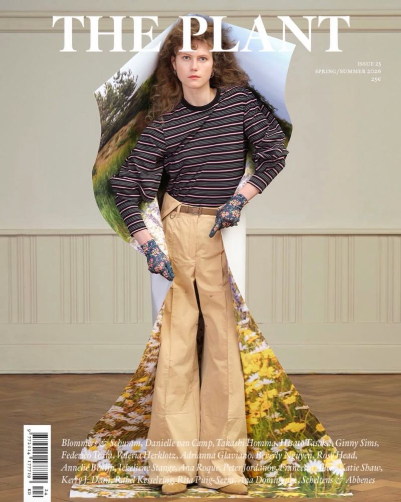 Magazine cover featuring woman with long brown hair wearing striped shirt and khaki pants, posing with landscape print backdrop.