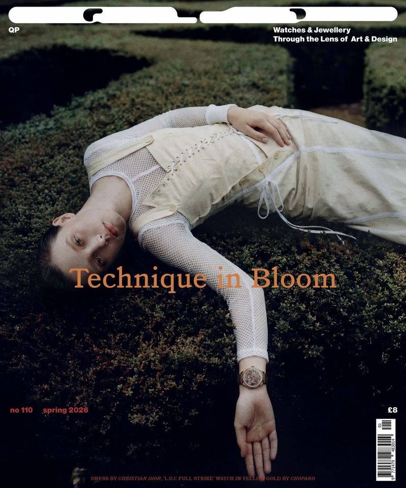 Model lying back on dark green garden foliage wearing a cream dress and gold wristwatch for an editorial magazine cover.