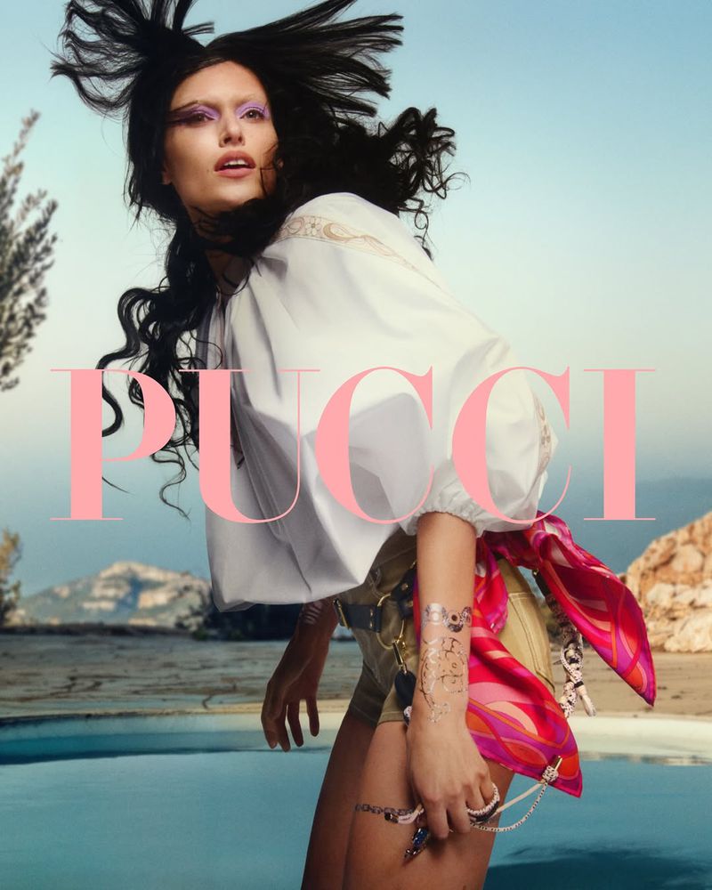 A woman poses in a fashion shot with a light blue sky and mountain background, showcasing a white top and patterned shorts. The word 'PUCCI' is overlaid.