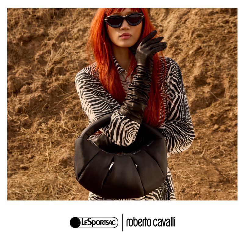 Fashion shot featuring an adult female model with red hair wearing zebra-patterned blouse, black gloves, and holding a black purse against brown background.