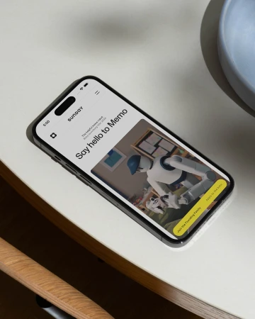 Smartphone displaying the Sunday Robotics mobile interface on a white tabletop next to a wooden chair.