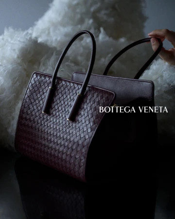 Bottega Veneta woven burgundy leather tote bag held by hand against a soft white textured background.