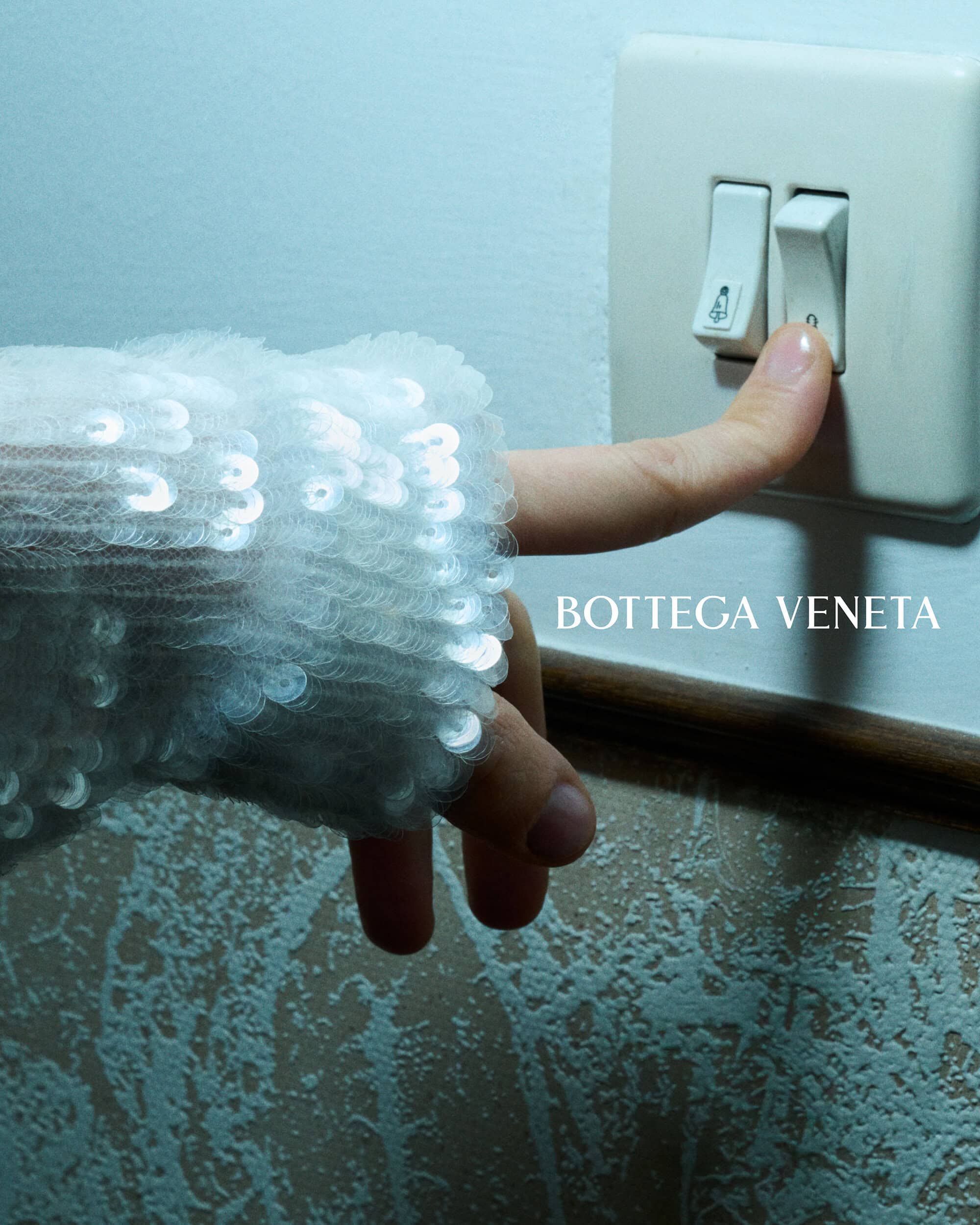 Close-up of a hand wearing a white sequin cuff pressing a white wall light switch against an interior wall.
