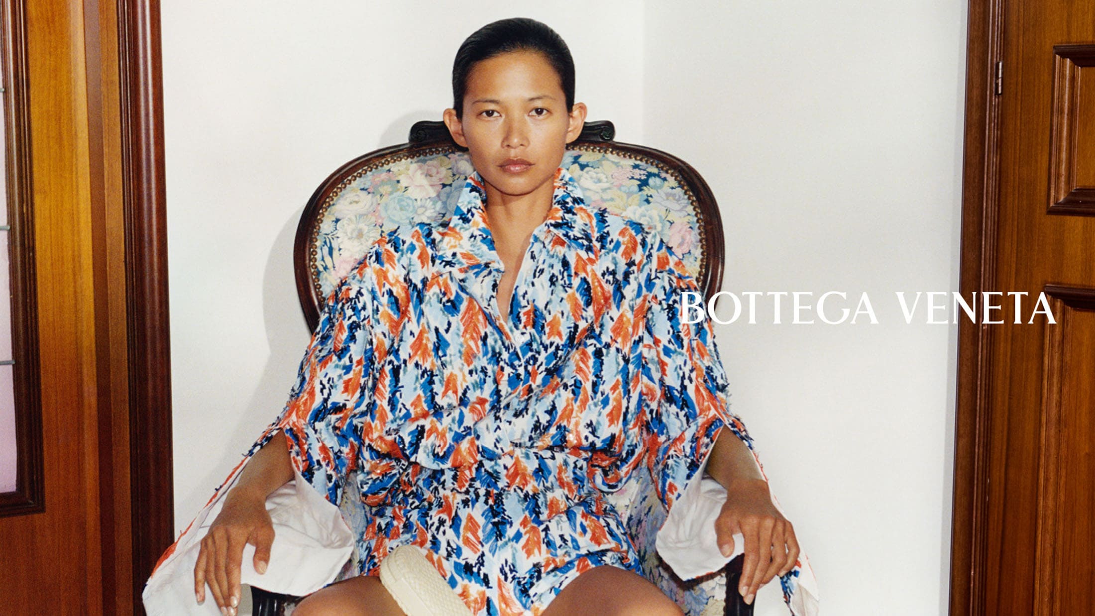 Model seated in an ornate patterned armchair wearing a blue patterned outfit for Bottega Veneta Fall 2026