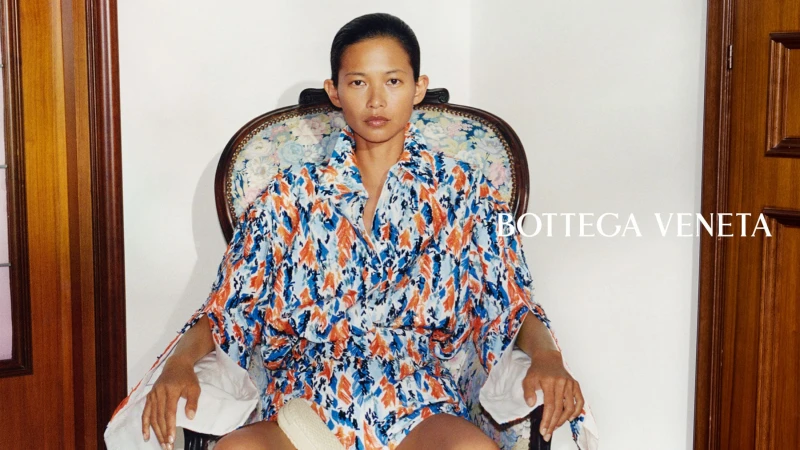 Model seated in an ornate patterned armchair wearing a blue patterned outfit for Bottega Veneta Fall 2026