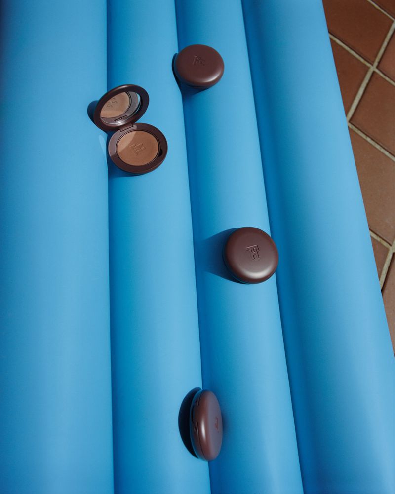 Beauty product bronzer compacts arranged on a blue inflatable pool surface. Cosmetic and summer lifestyle product photography.